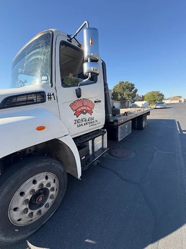 White flatbed tow truck parked on asphalt with clear blue sky