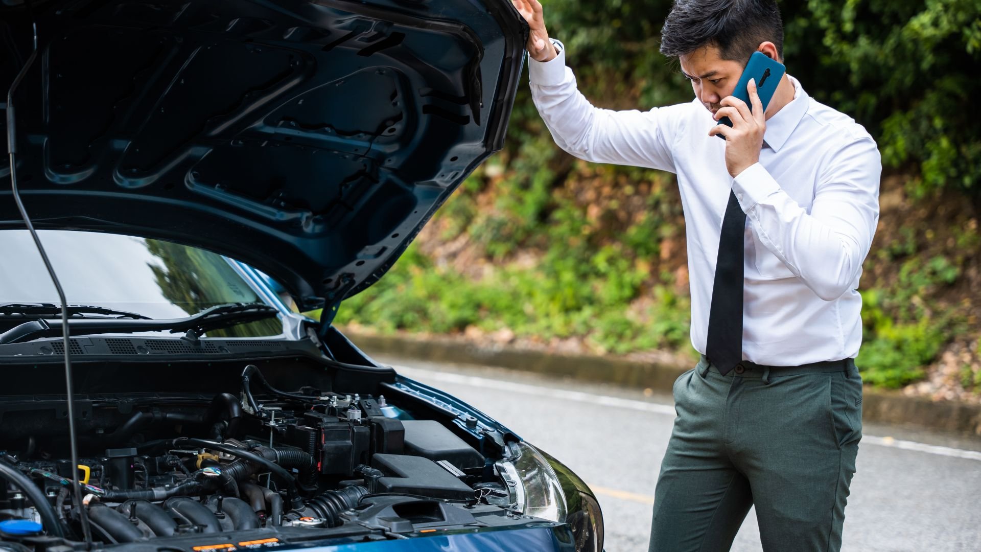 Man in business attire calling for help with broken down car