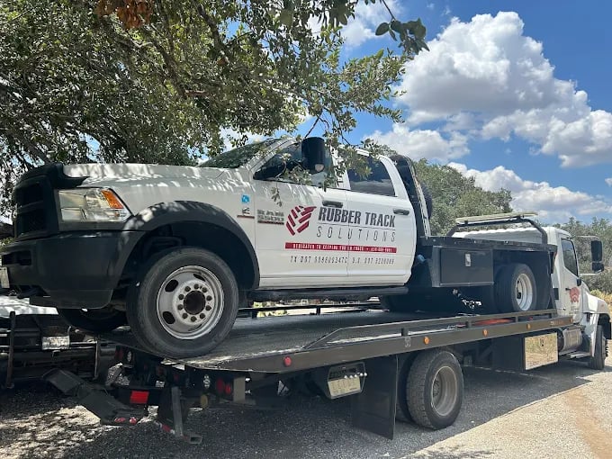 White Rubber Track Solutions truck loaded on a flatbed tow truck