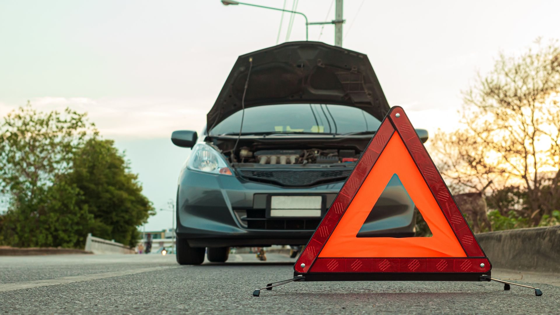 Broken down car with open hood and warning triangle on roadside