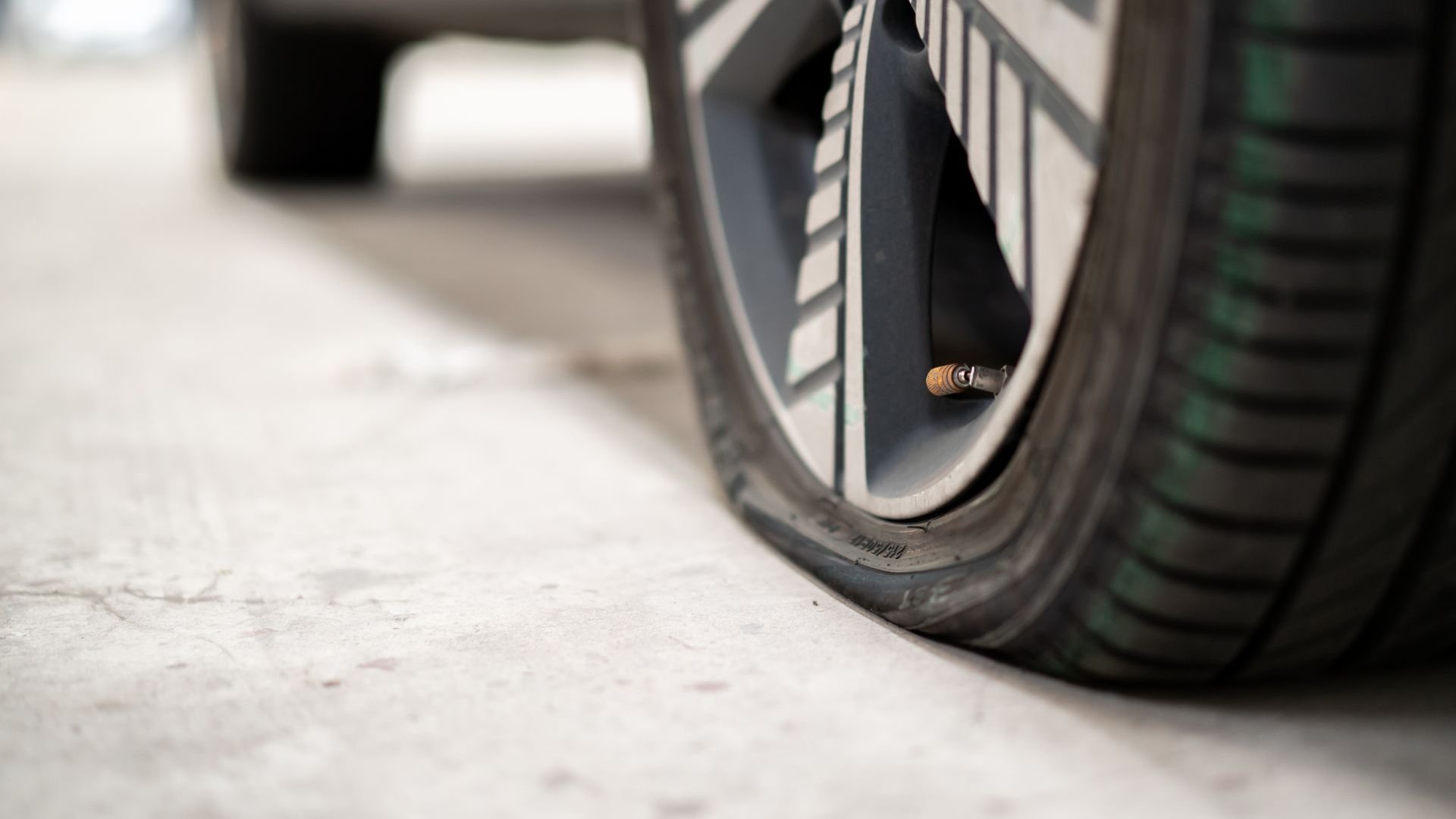 Flat car tire with visible valve stem on light-colored surface