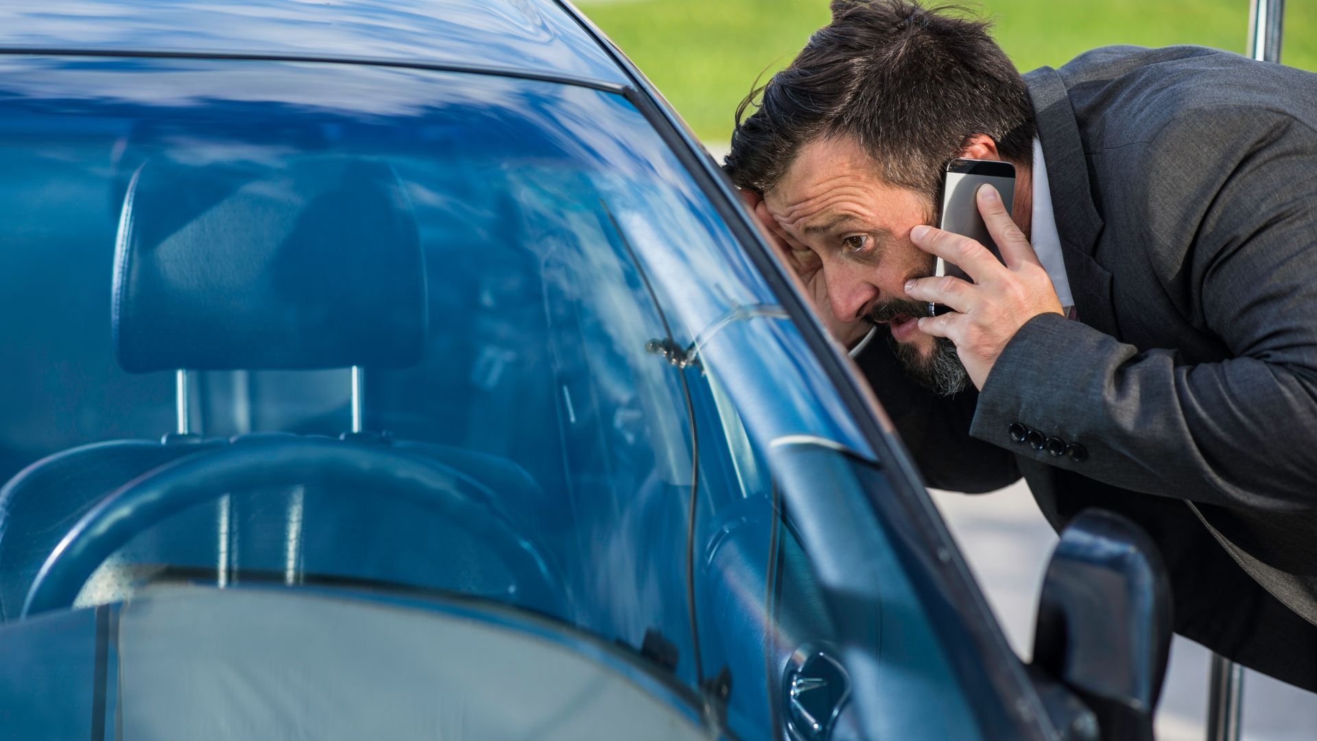 Frustrated businessman making a phone call near blue car window