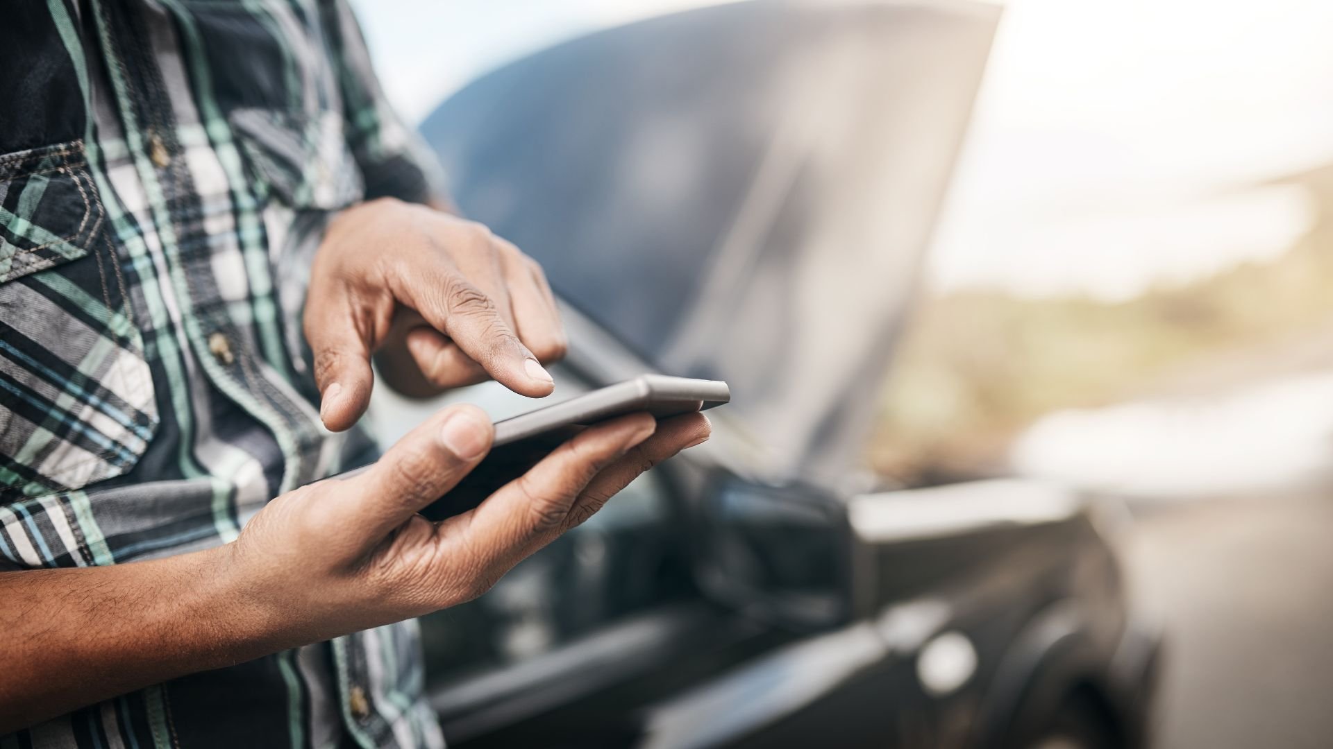 Person in plaid shirt using smartphone near car with blurred background