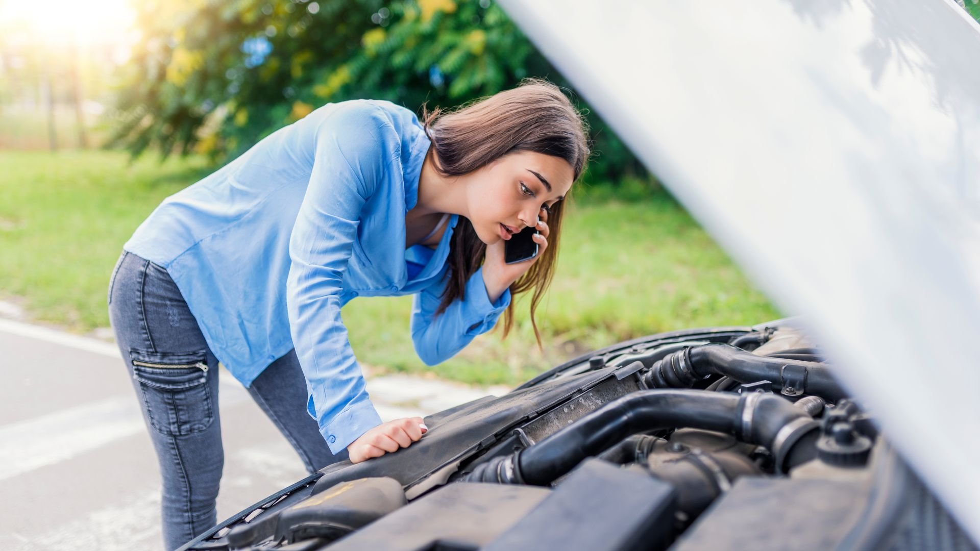 Woman checking car engine while calling for roadside assistance