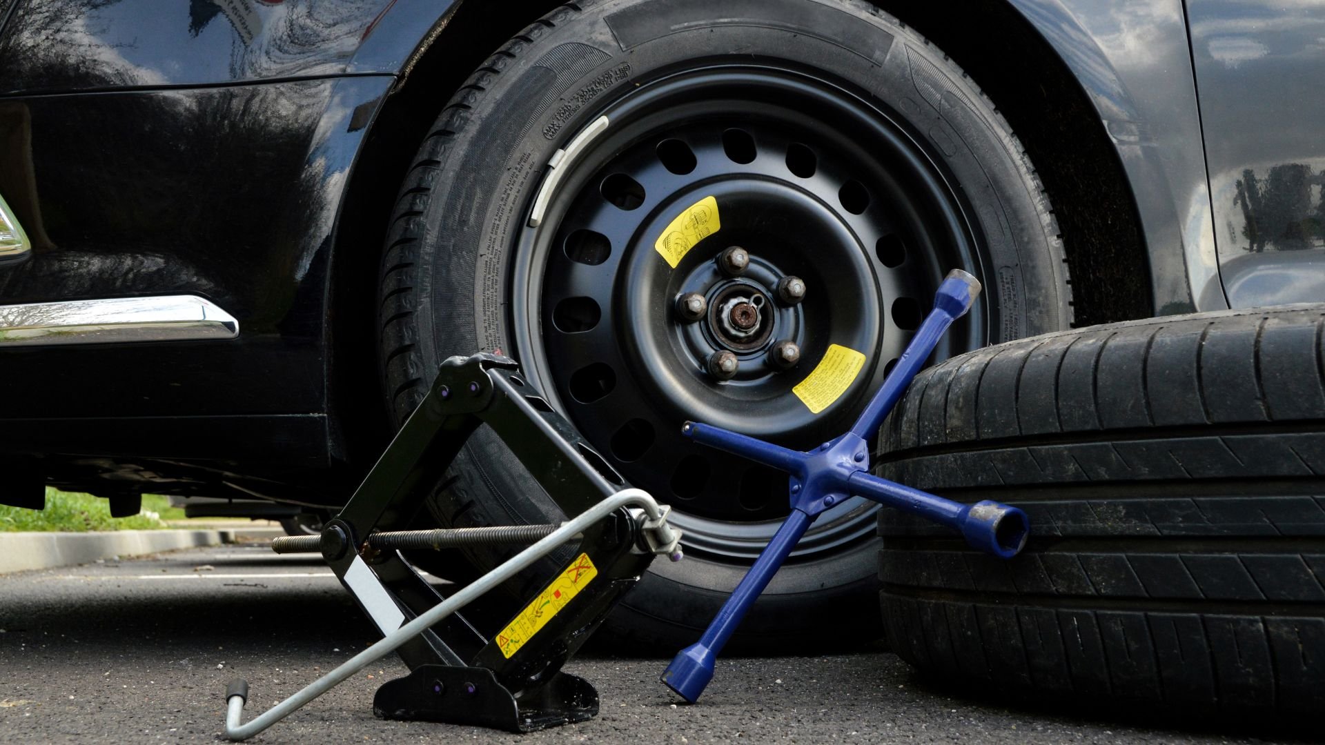 Car tire being changed with jack and lug wrench on asphalt