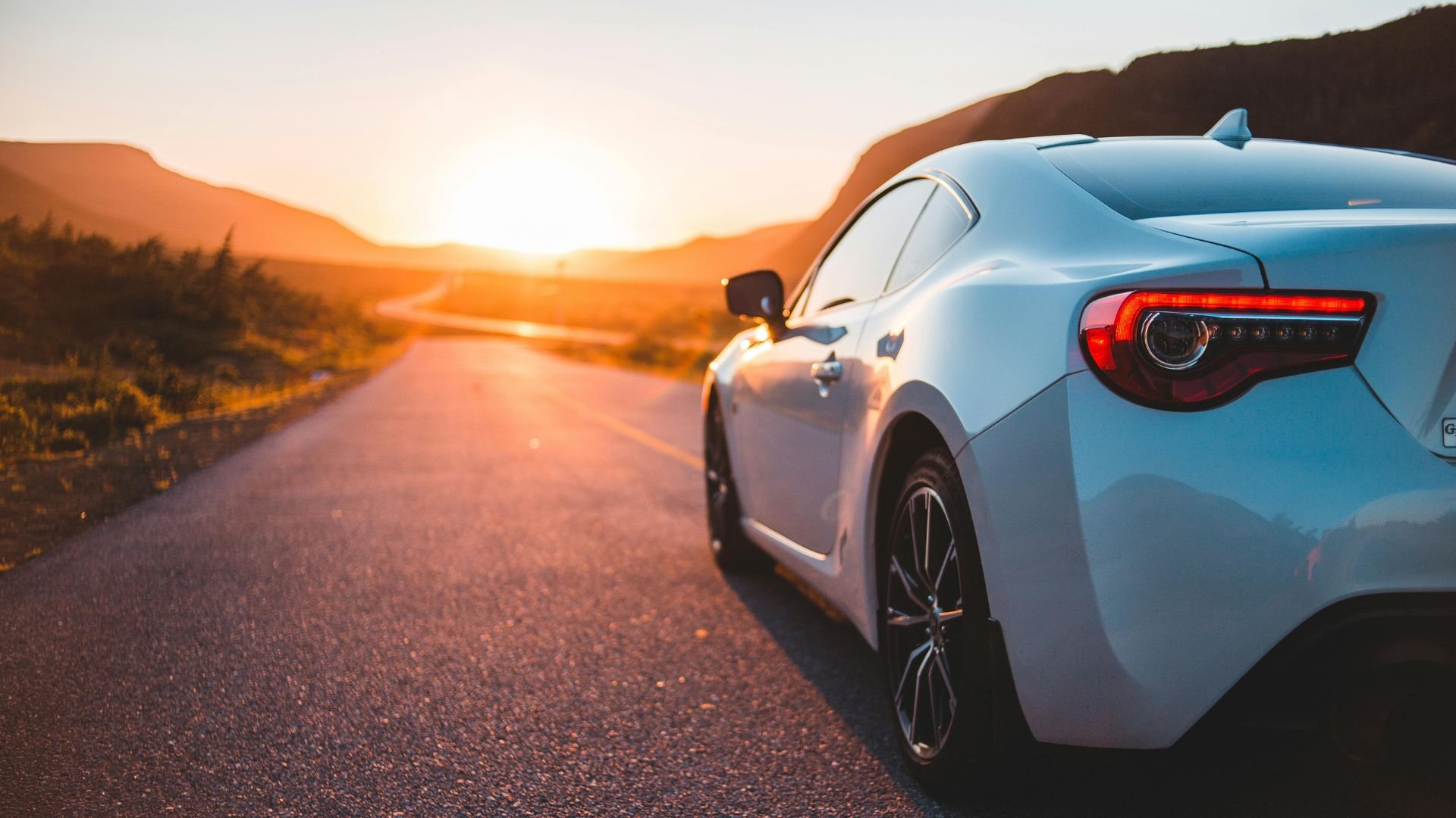 Silver sports car parked on winding road during golden sunset