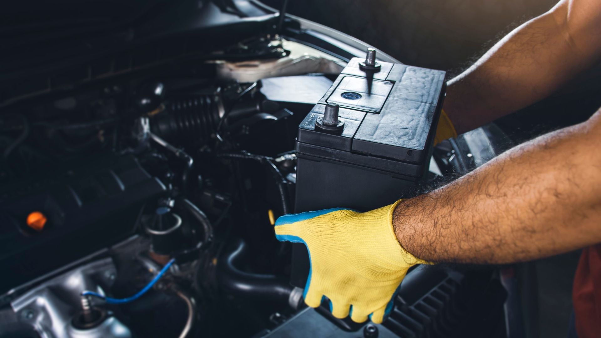 Mechanic with yellow glove checking car battery in engine compartment