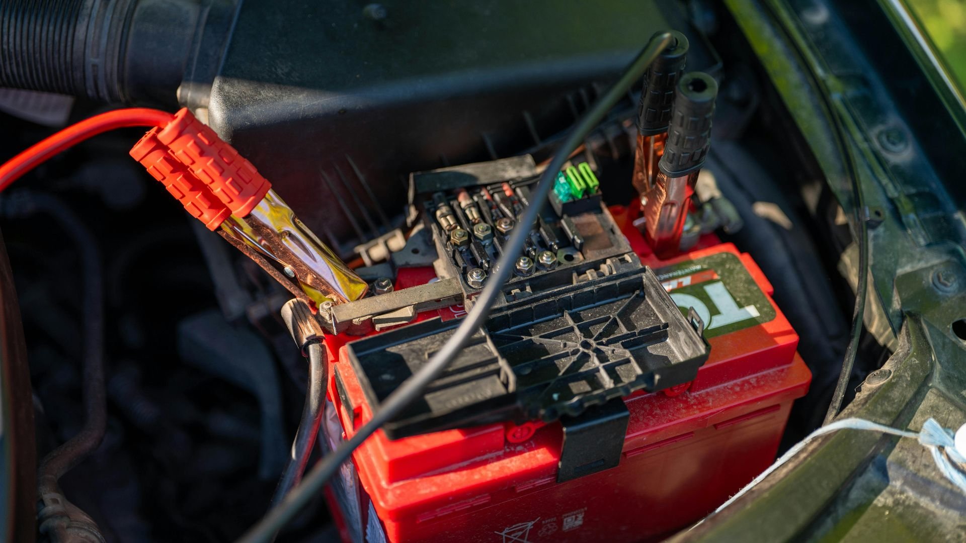 Red car battery with jumper cables connected in engine compartment