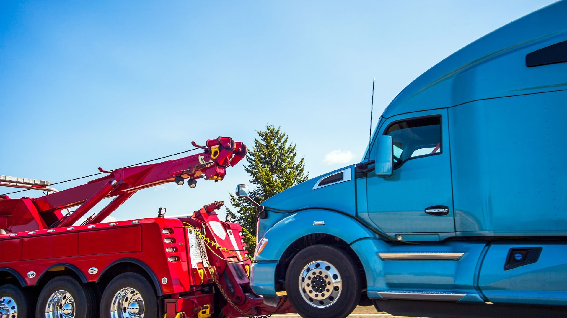 Red tow truck preparing to tow a blue semi-truck on a clear day