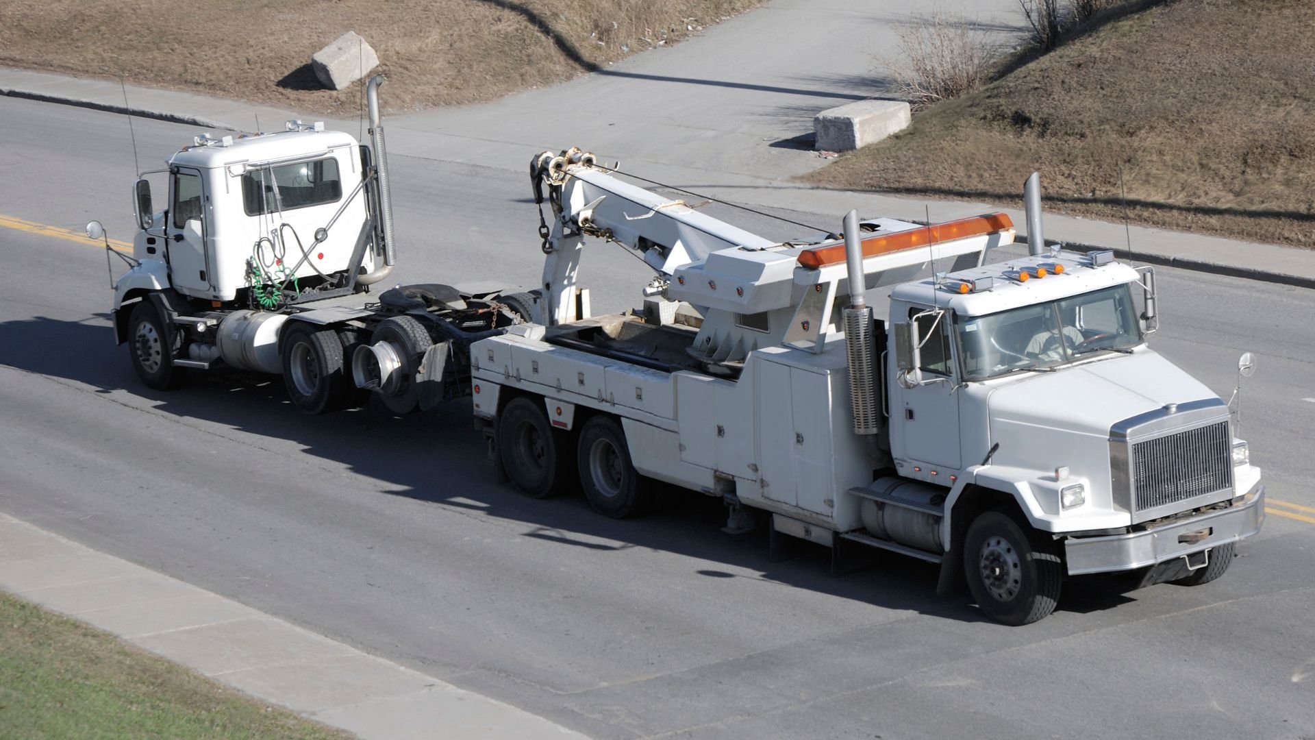 White tow truck pulling another truck on a highway roadway