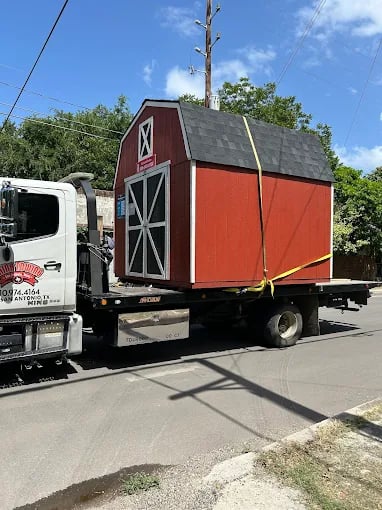 Red shed being transported on a flatbed truck on a sunny day