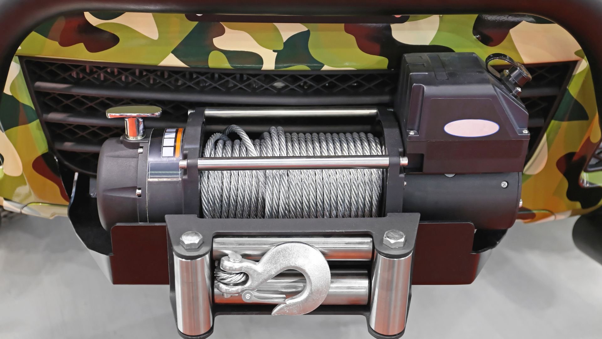 Heavy-duty winch with steel cable mounted on camouflage background